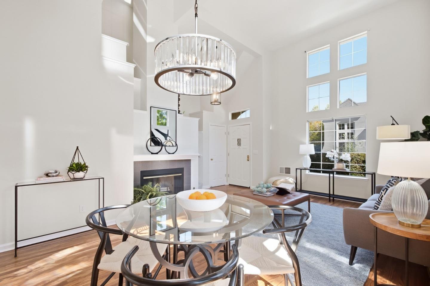 Staged living and dining room with vaulted ceiling, tall windows, fireplace, and circular chandelier.