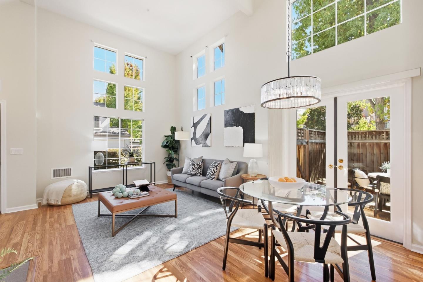 Double-height living and dining room with tall windows, a gray sofa, and French doors to a patio.