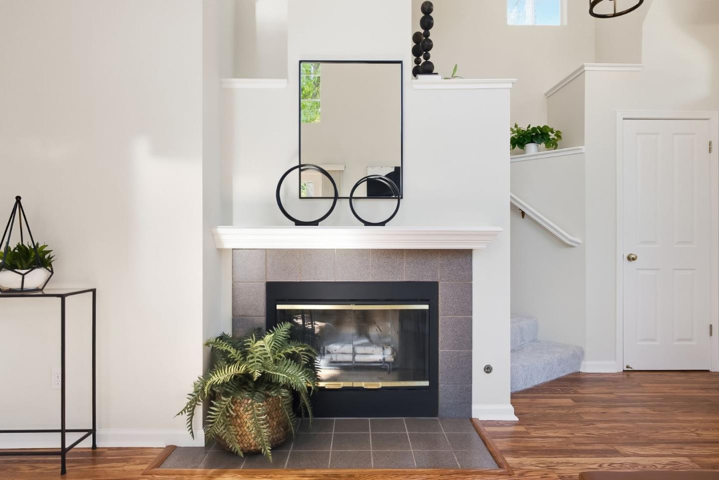 Living room fireplace with a large mirror, hardwood floors, and a staircase.