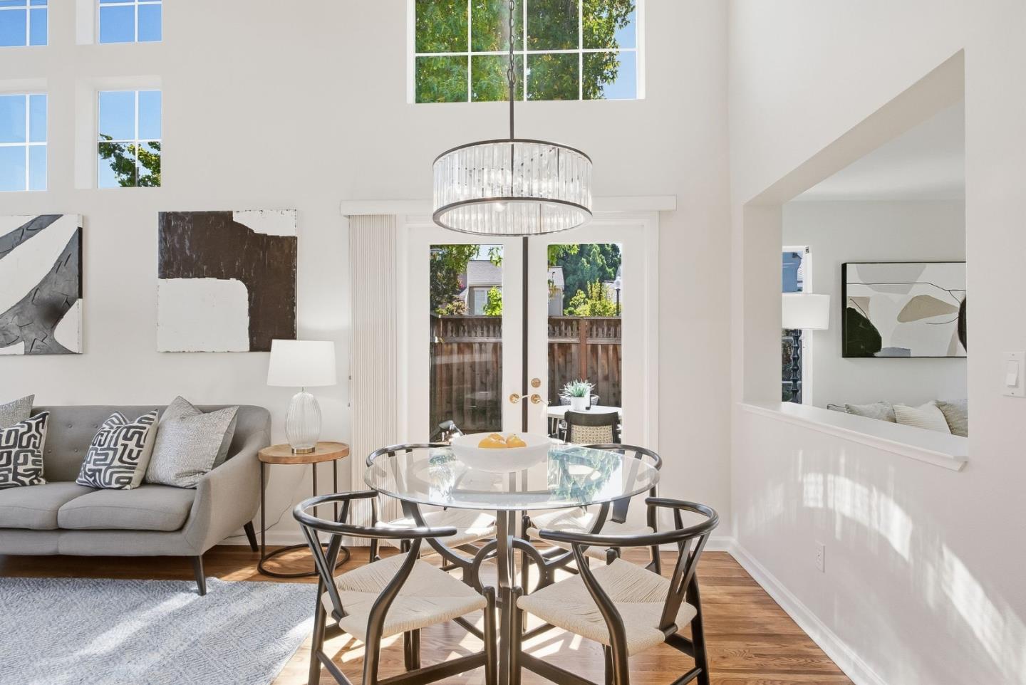 Dining area with a glass-top table and chairs beside a gray sofa and tall windows.