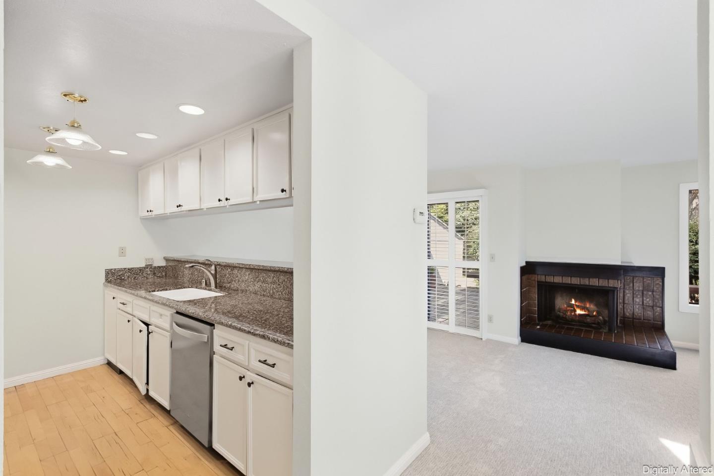 Kitchen and living room with speckled counters, stainless dishwasher, and a tiled fireplace.