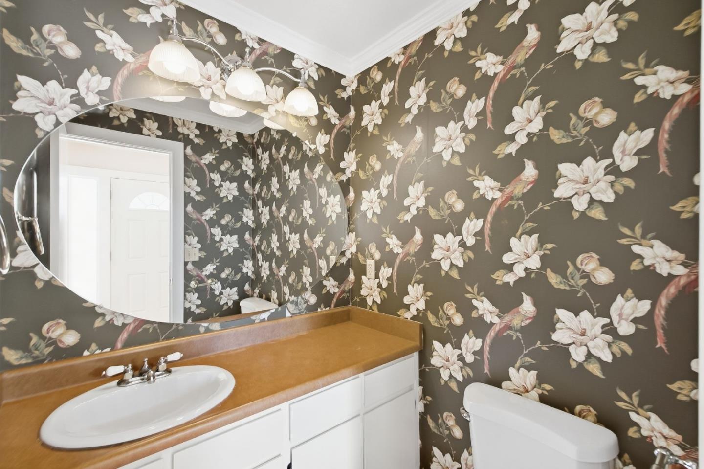 Bathroom with bold floral wallpaper, a tan vanity countertop, and a white bathtub.