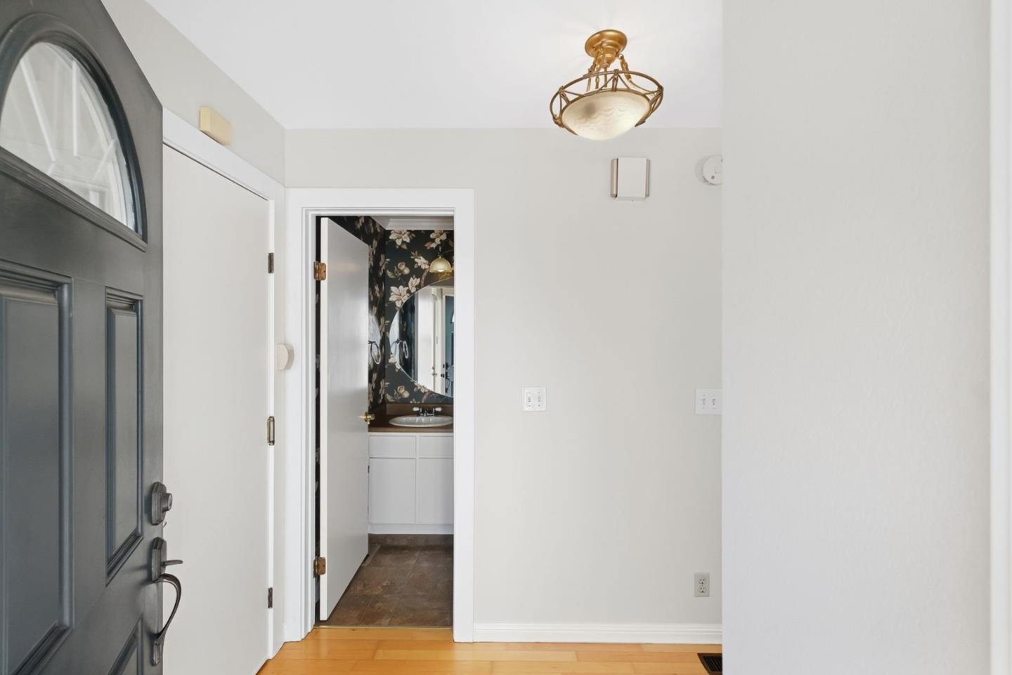 Entry foyer with a dark front door and a view into a floral-wallpapered bathroom.