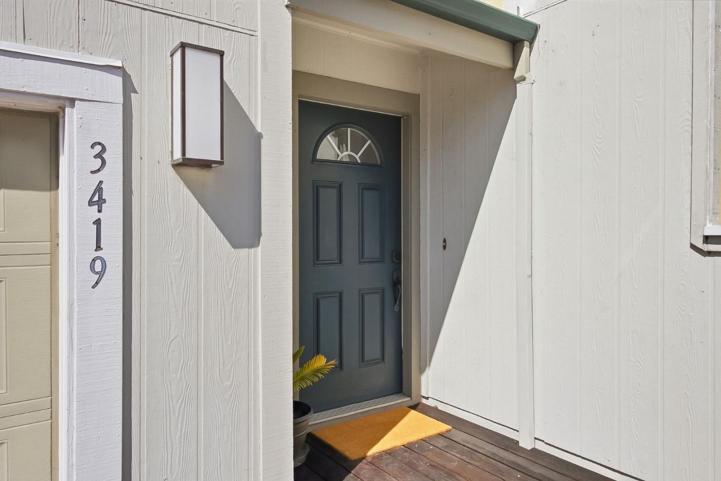 Recessed dark front door with a semicircular window, yellow doormat, and house number 3419.