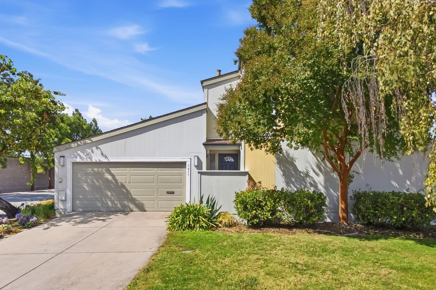 Split-level home with a double garage, yellow siding, and a large tree shading the front lawn.