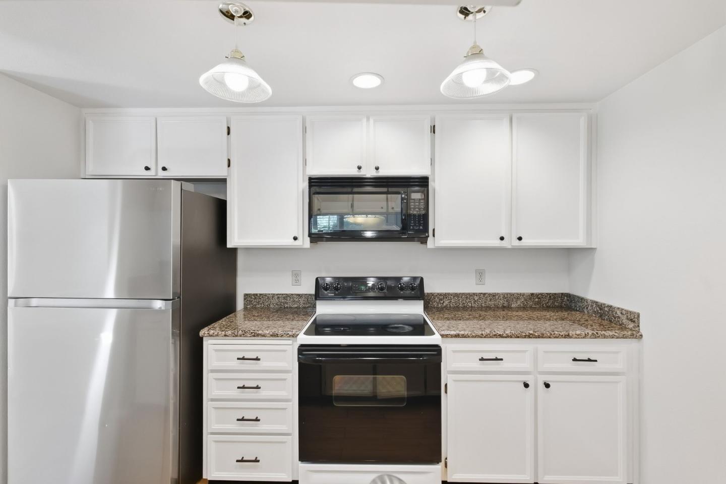 Kitchen with white cabinets, speckled countertops, and stainless-steel refrigerator beside a black range.