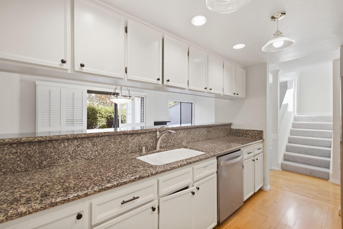 Kitchen with granite counters, white cabinetry, stainless dishwasher, and a carpeted staircase.