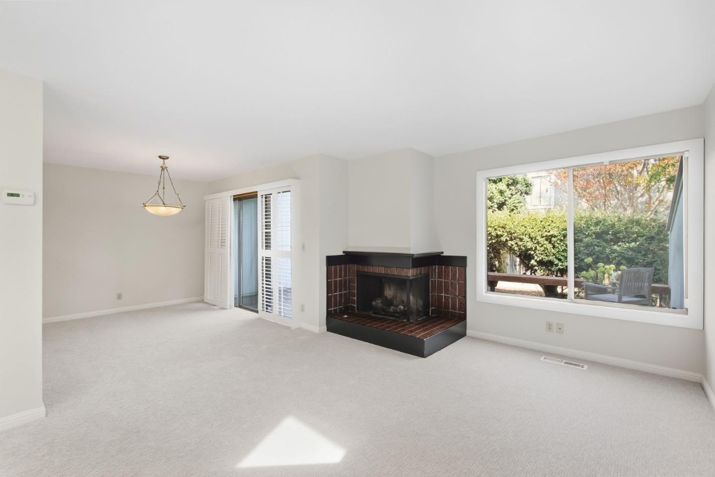 Vacant living room with a brick corner fireplace and a large garden-facing window.