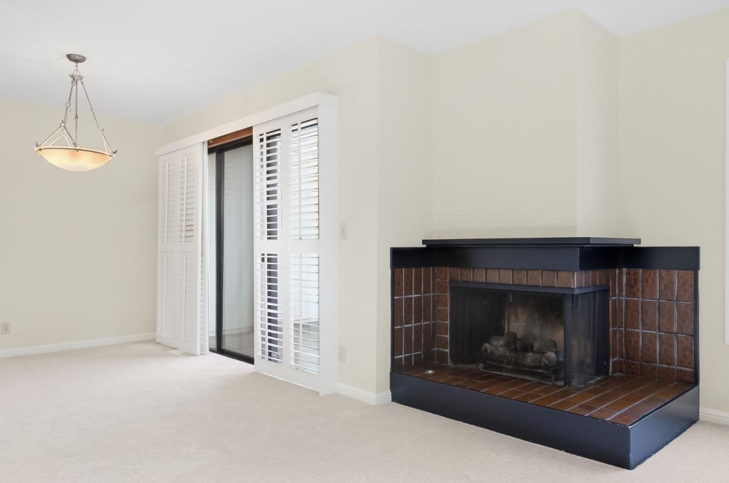 Empty living room with a tiled corner fireplace and white plantation shutters.