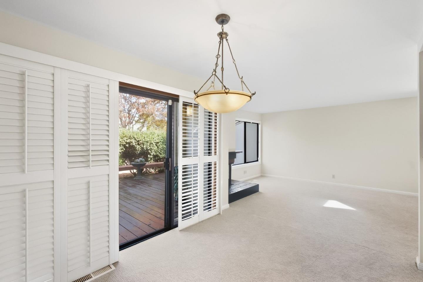 Empty carpeted living room with plantation shutters and a sliding door to a wood deck.