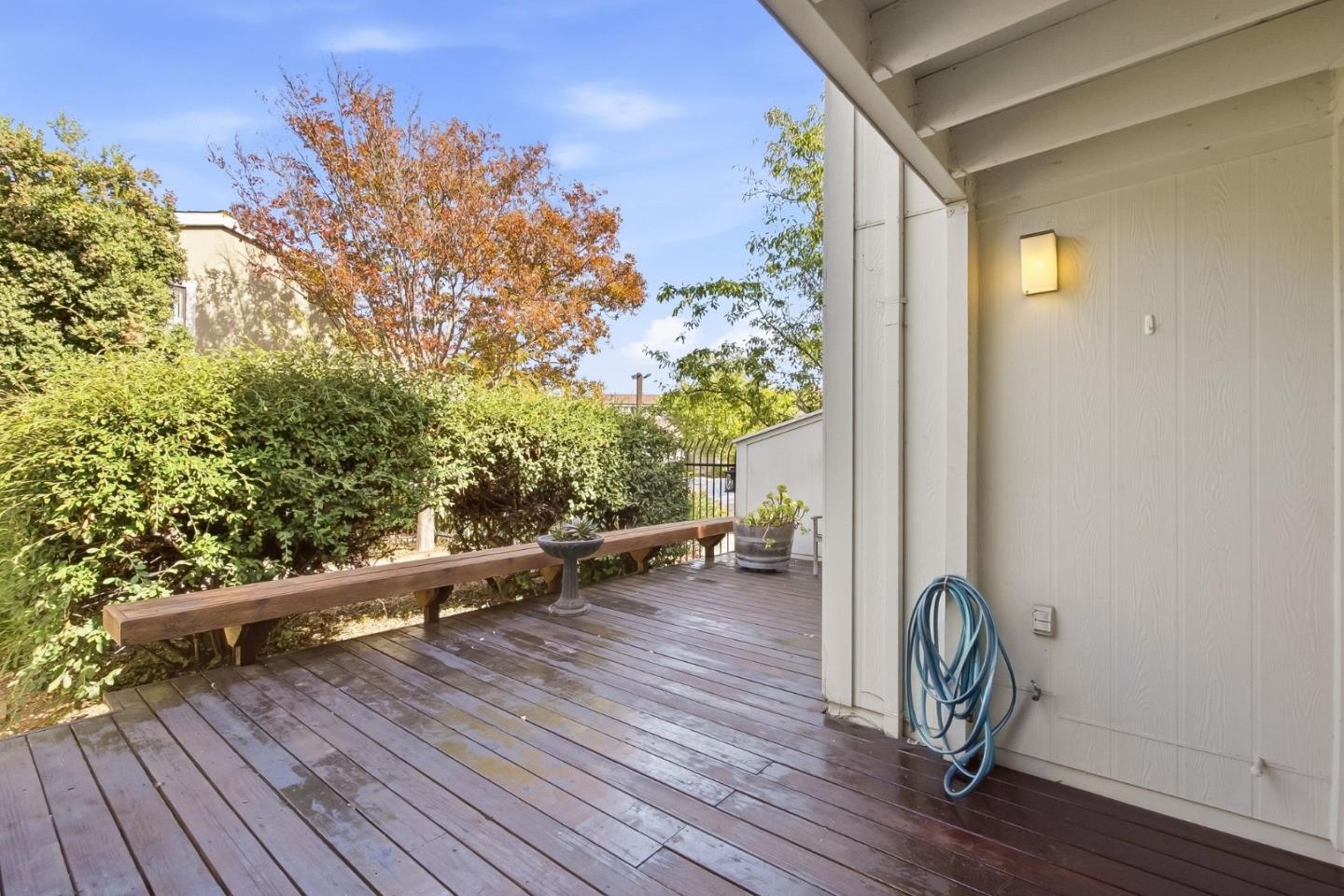 Wooden deck beside the house, with a long bench, potted plants, and hedge.