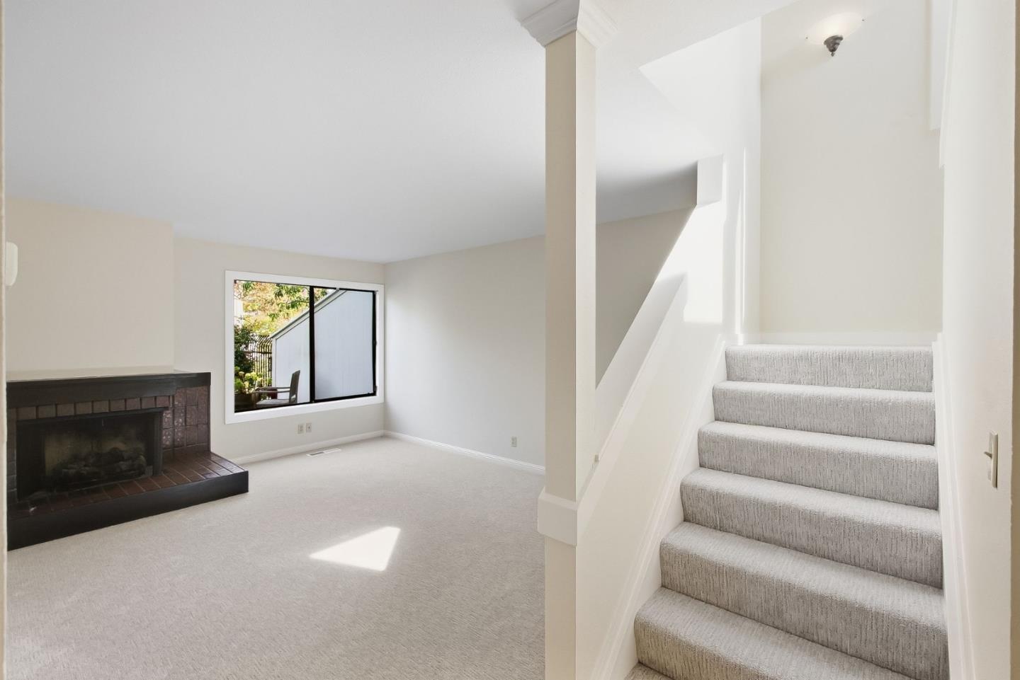 Vacant living room with a dark brick fireplace and staircase beside a large window.