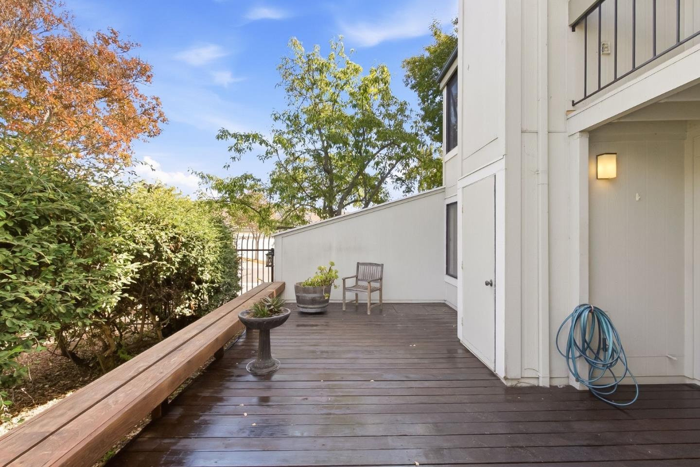 Wooden deck beside a white home, with potted plants, a chair, and a coiled garden hose.