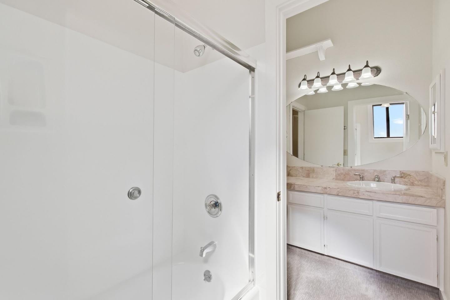 Bathroom with glass shower, double-sink pink marble vanity, and large oval mirror.