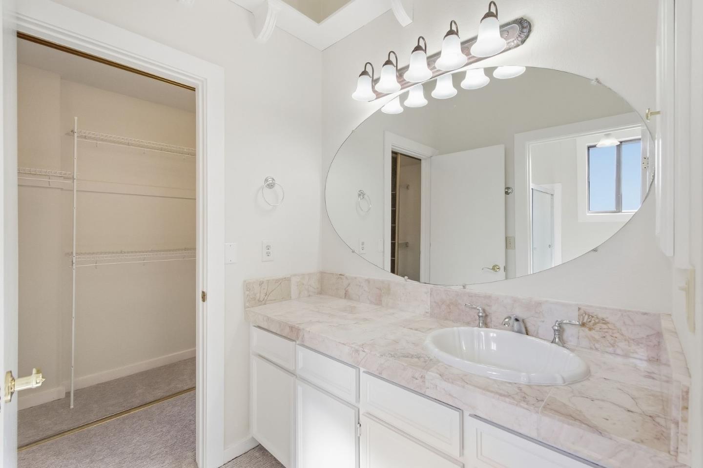 Bathroom with a marble vanity and oval mirror beside an open walk-in closet.