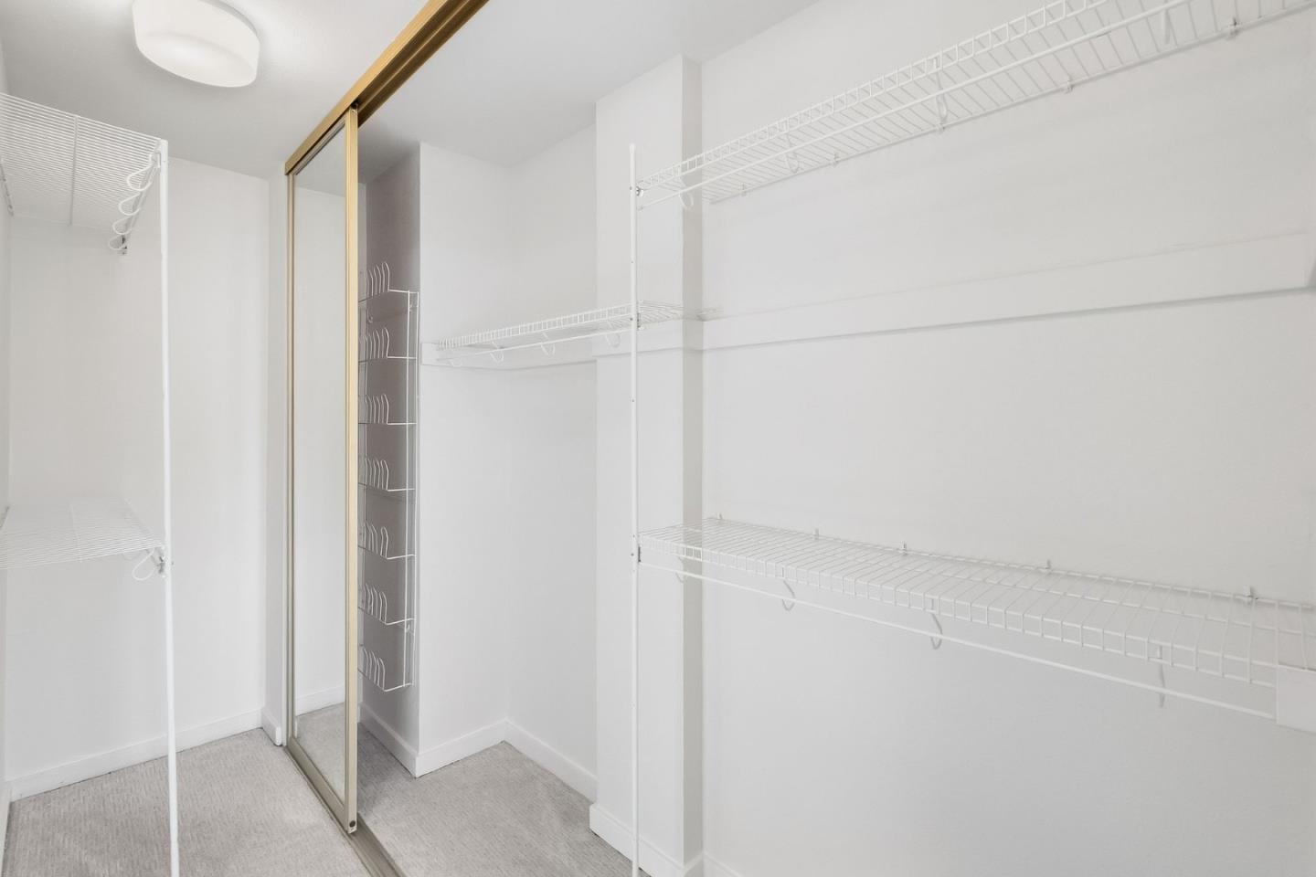 Walk-in closet with white wire shelves, gray carpet, and a mirrored sliding door.