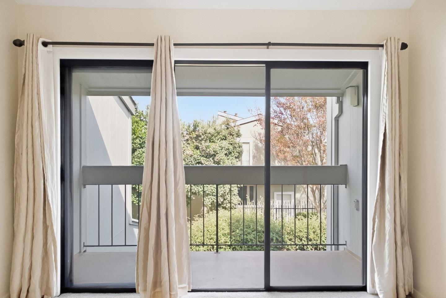 Sliding glass doors open to a covered balcony with a black railing and leafy greenery beyond.