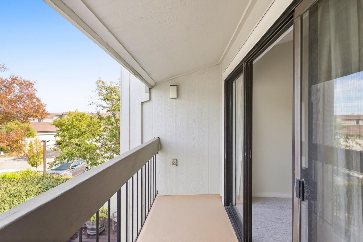 Covered balcony with black railing and sliding glass doors overlooking trees and neighboring homes.