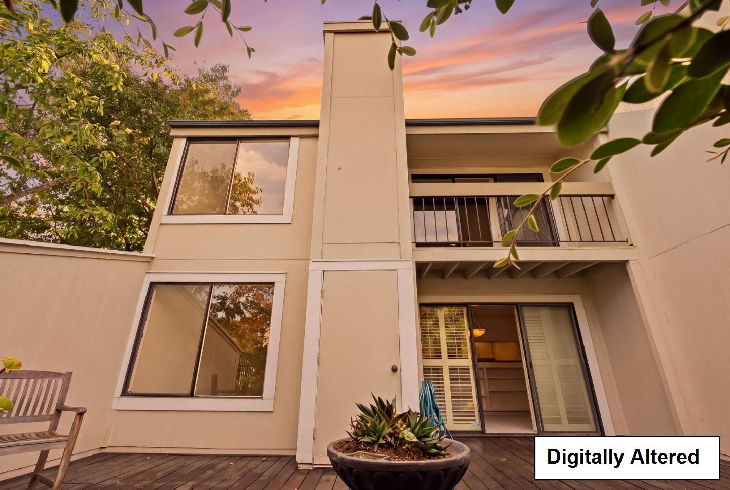 Two-story home exterior with a balcony and wooden patio deck at sunset.