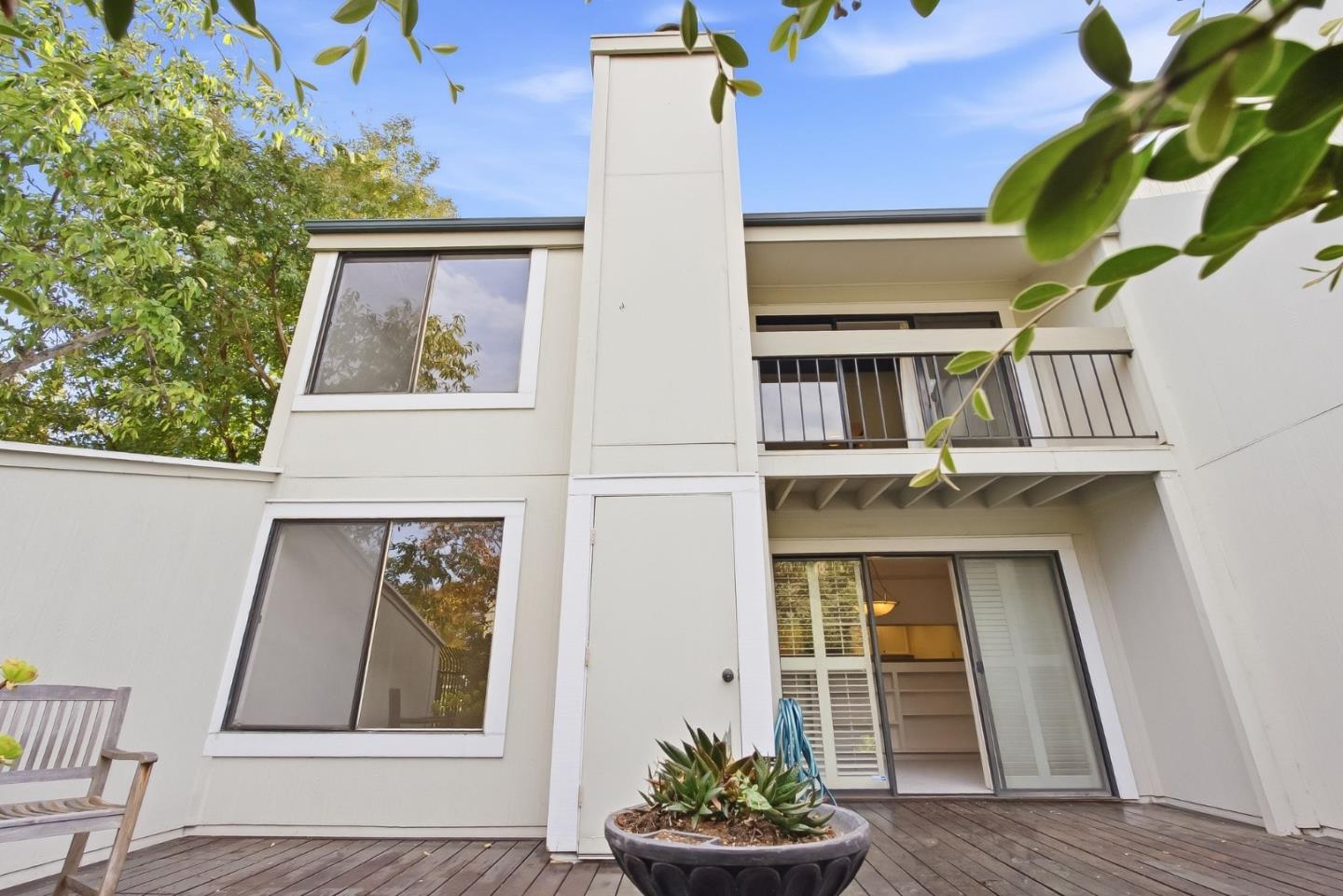 Two-story home with an upper balcony, wooden deck, and succulent planter in the courtyard.