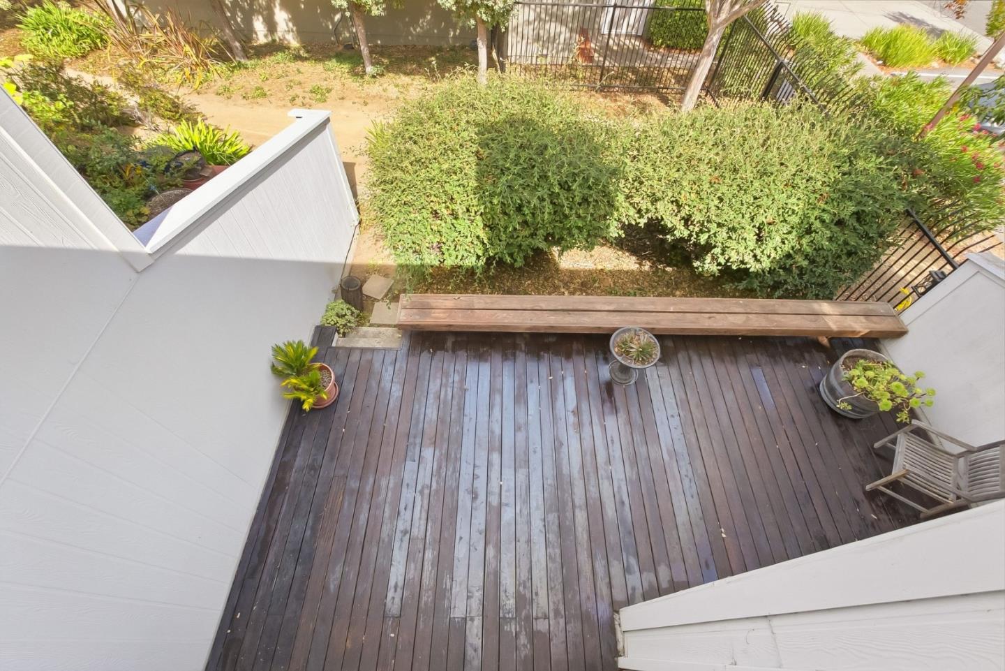 Wooden deck with a long bench, potted plants, and a leafy hedge garden.