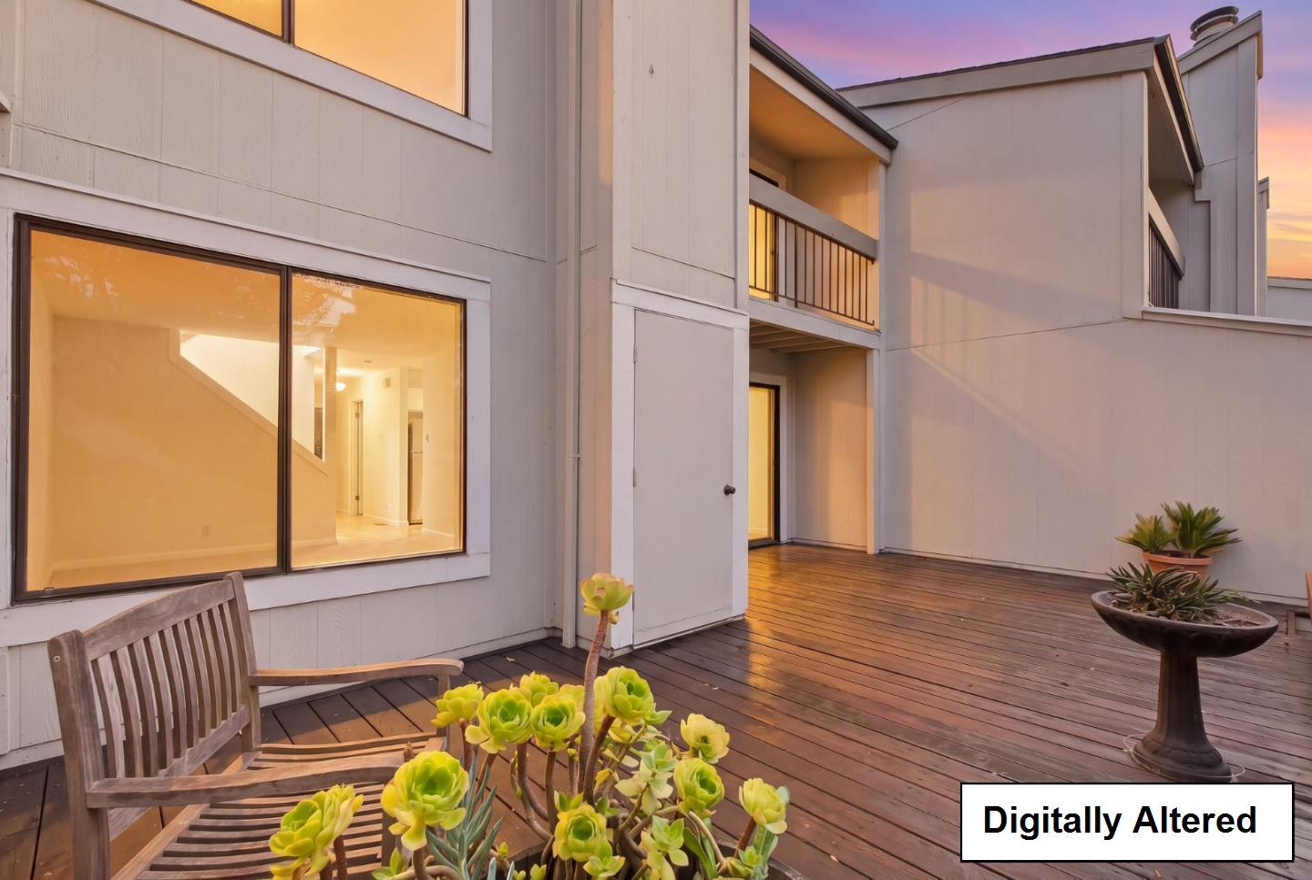 Modern home’s wooden deck with sliding glass doors, an upper balcony, and potted succulents at sunset.
