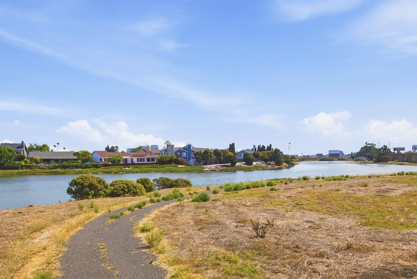 Waterway with homes across the bank and a paved path along the dry shoreline.