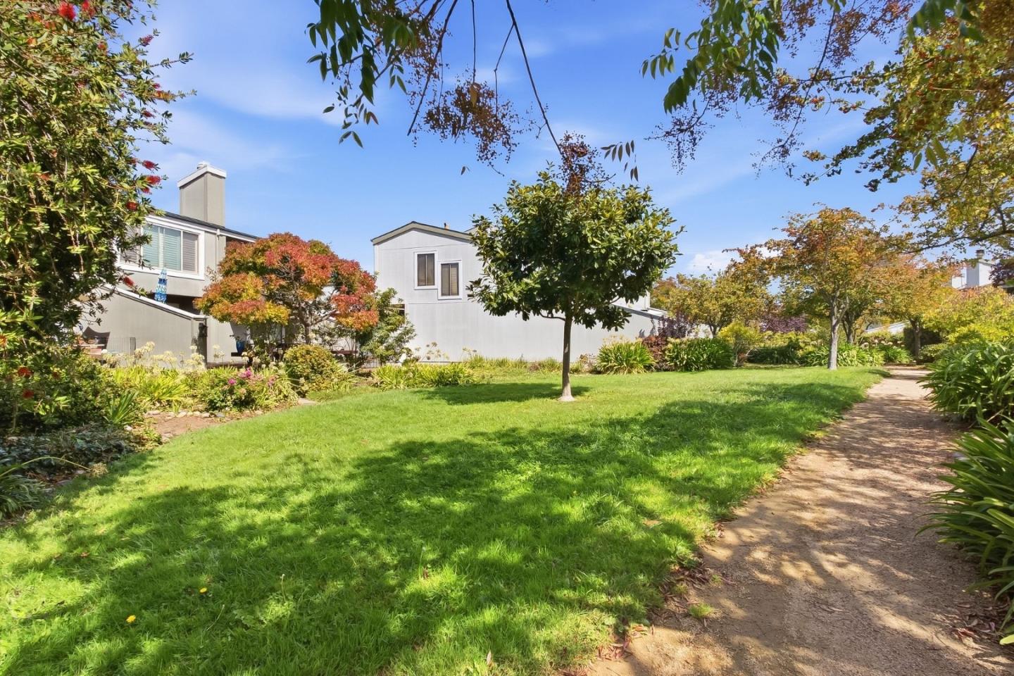 Modern gray home behind a landscaped lawn with mature trees and a curving garden path.