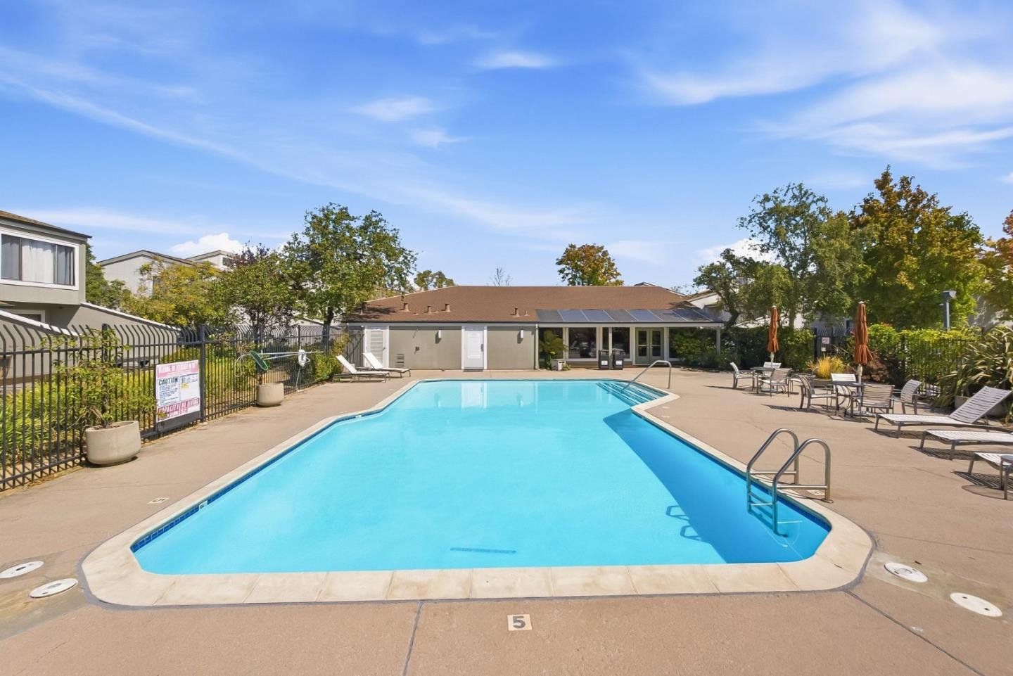 Residential complex pool with a fenced deck, lounge chairs, and a low building behind it.