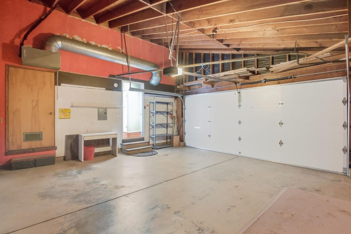 Vacant garage with exposed ceiling joists, concrete floor, and a large white garage door.