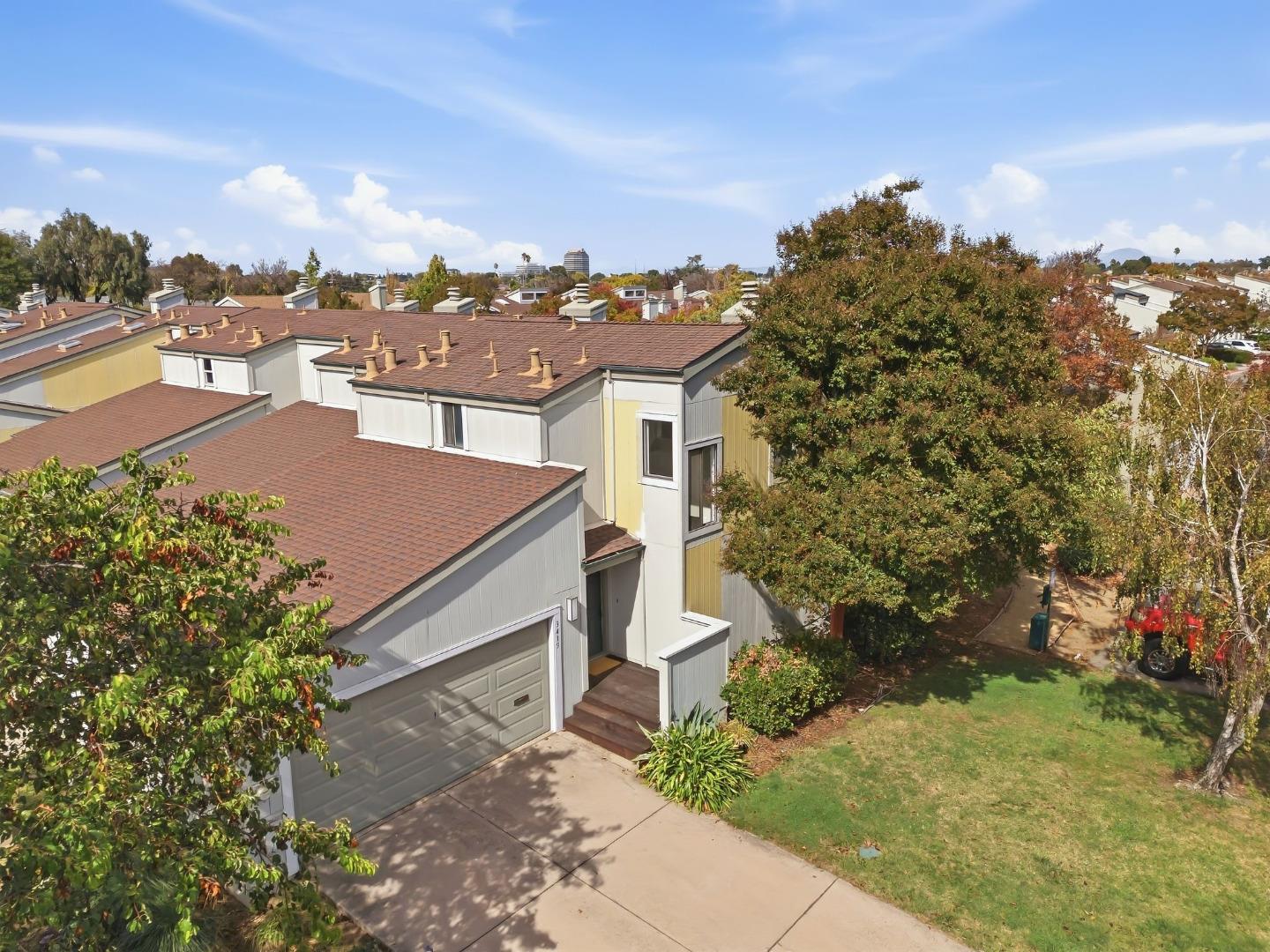 Townhouse with an attached garage and driveway, viewed from above among leafy trees.