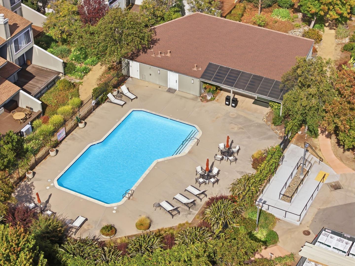 Outdoor swimming pool with lounge chairs, patio tables, landscaping, and solar panels on the adjacent roof.