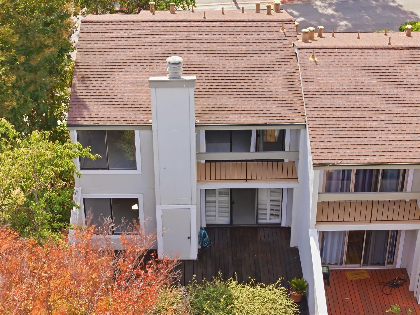 Townhouse exterior with shingle roofs, stacked balconies, and wood decks among leafy trees.