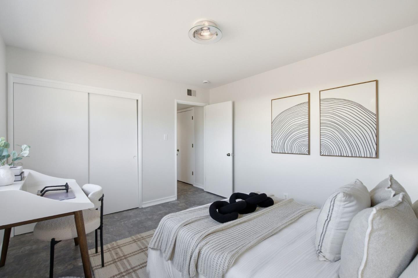 Staged bedroom with a white bed, desk, sliding closet doors, and abstract wall art.