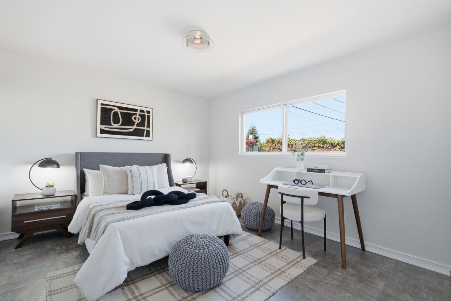 Staged bedroom with a gray upholstered bed, white desk, and wide window.
