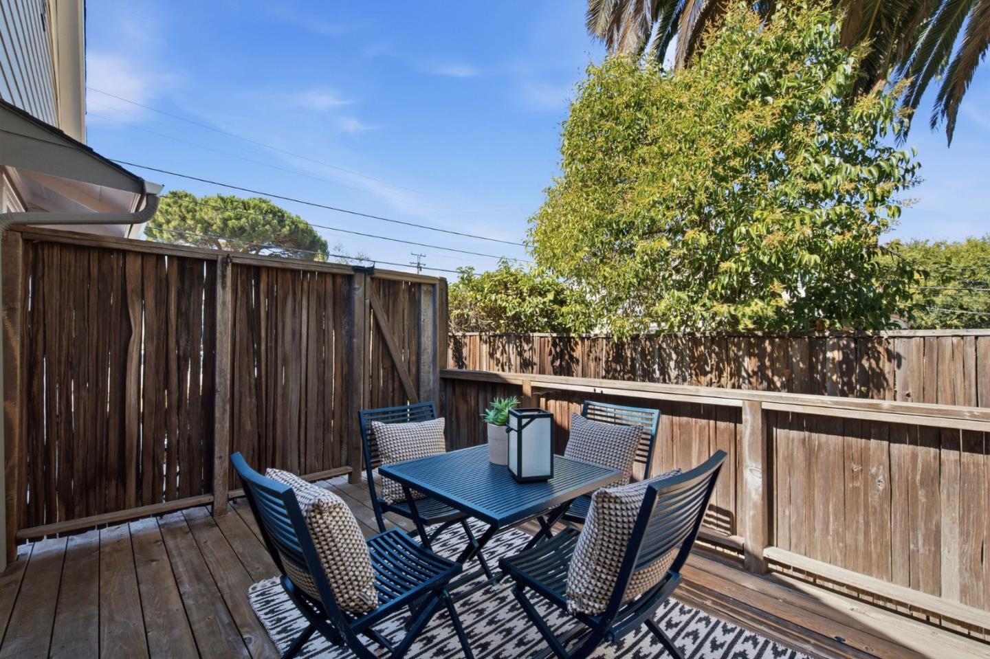 Wooden deck with a black outdoor dining set, tall privacy fencing, and leafy trees.