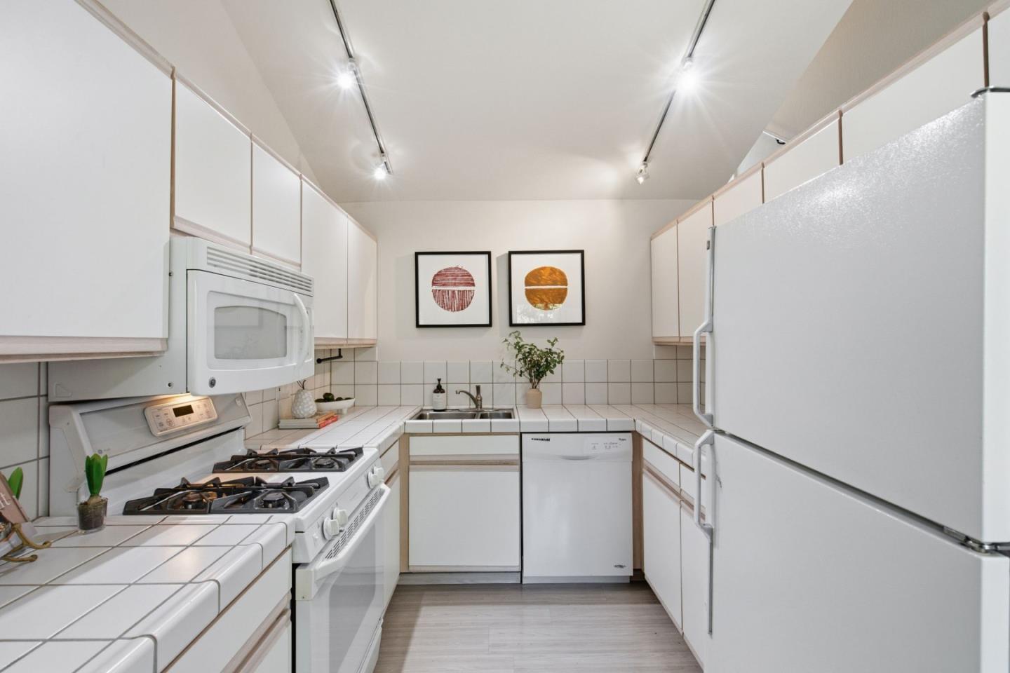 Kitchen with white cabinets, tiled counters, gas range, and a large refrigerator.
