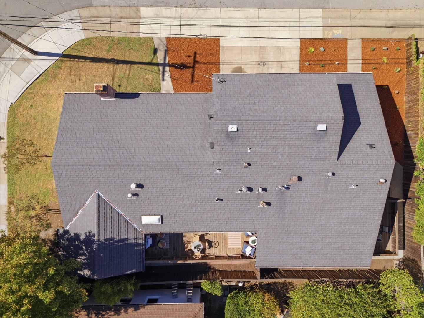 Aerial view of a home with a broad gray roof and a small deck with outdoor seating.