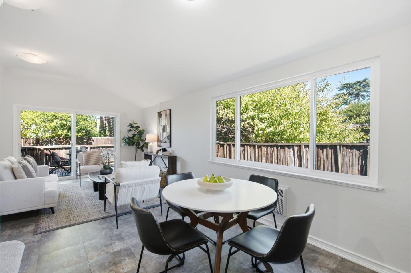 Furnished living and dining room with a round white table and large windows overlooking a fenced yard.