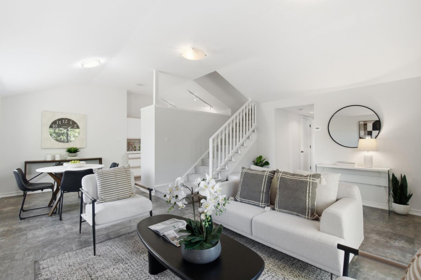Staged living and dining area with white sofas, a dark coffee table, and a staircase.