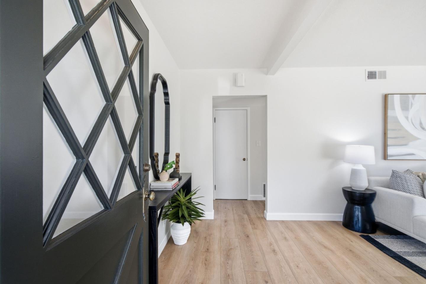 Staged entryway with a black glass-paneled door, light wood floors, and a view into the living room.