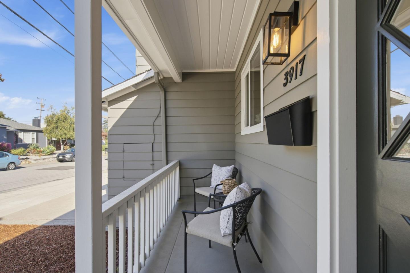 Covered porch with two cushioned chairs, white railing, and the number 3917 beside a wall lantern.