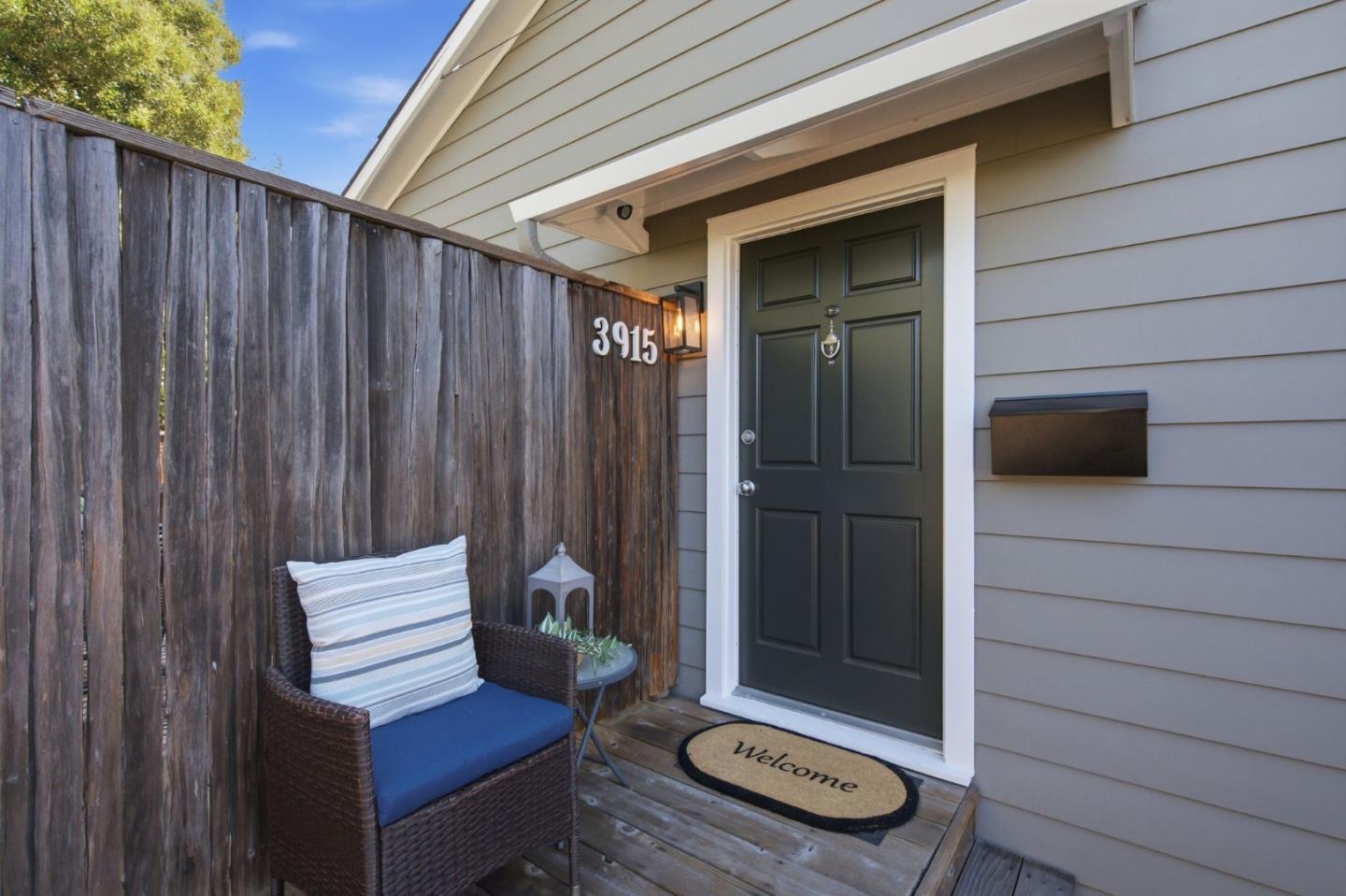 Home entrance with a dark green door, wooden privacy fence, and wicker seating on the porch.