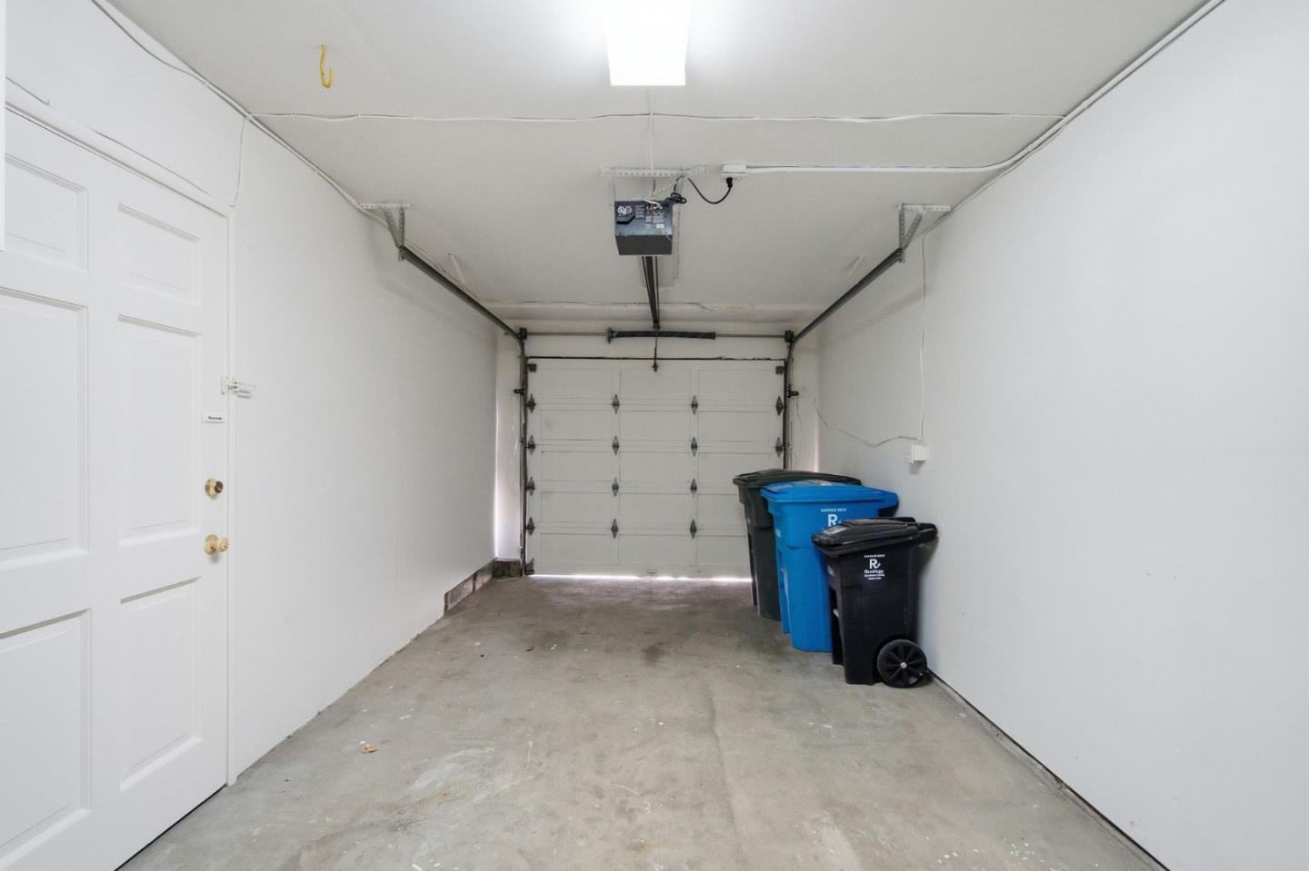 Empty garage with a concrete floor, closed garage door, and Recology bins along the right wall.