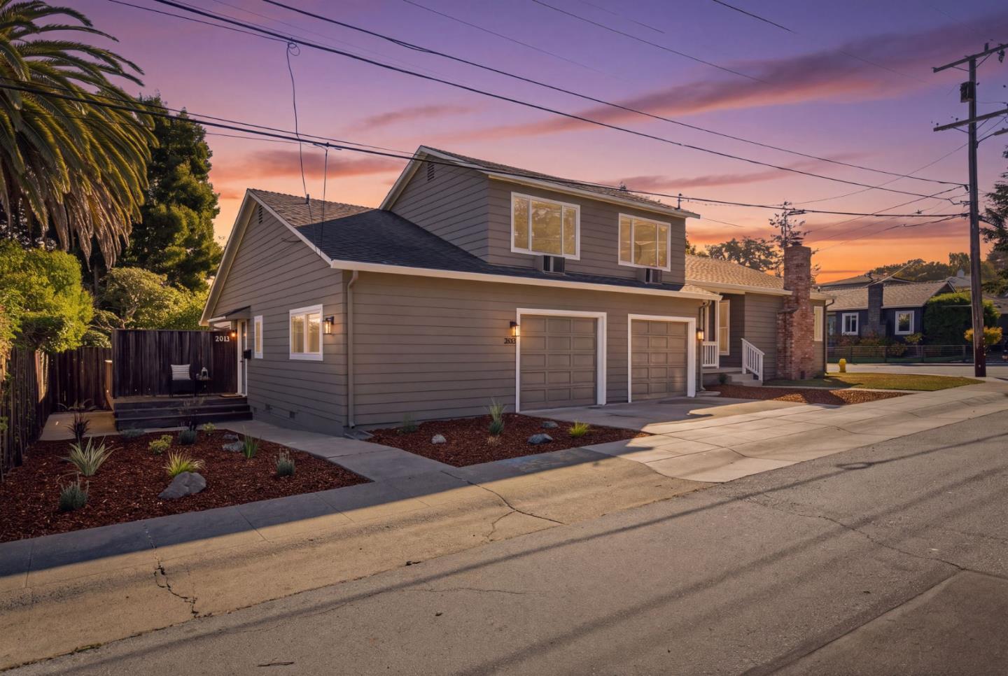 Two-story gray home with two garage doors and landscaped frontage at sunset.