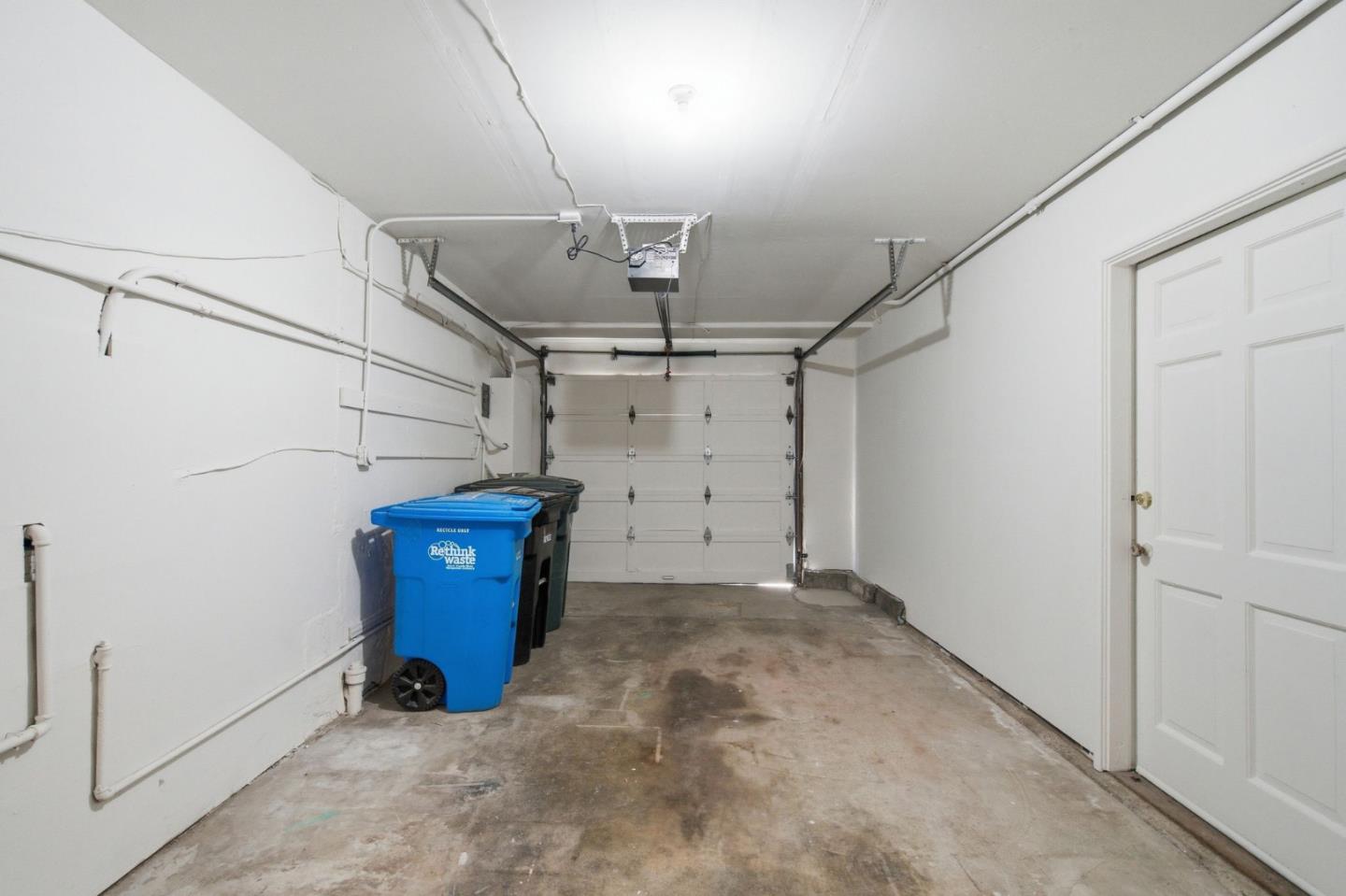 Residential garage with a concrete floor, overhead door, and recycling bins along one wall.