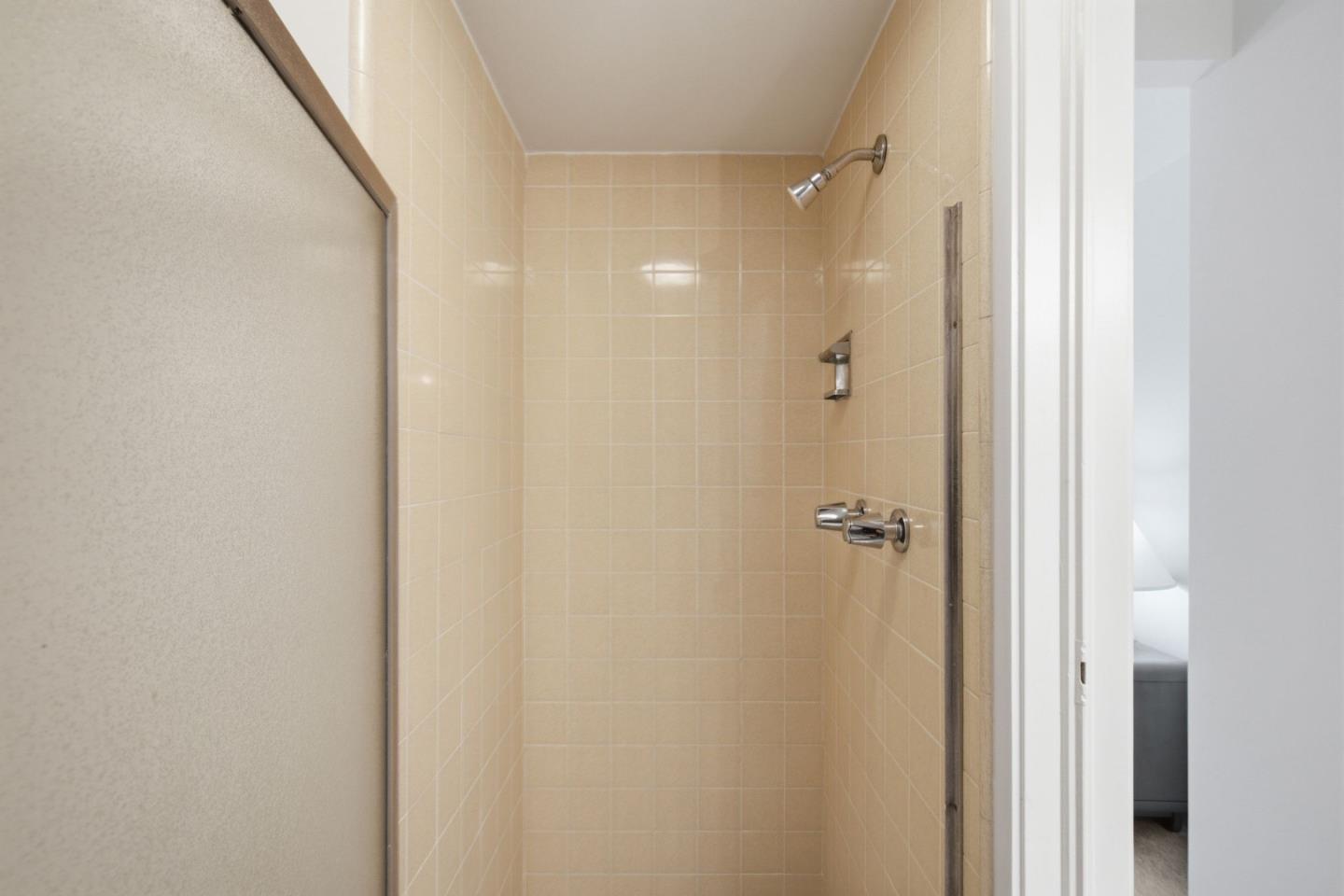 Tiled shower stall with beige walls and chrome fixtures.