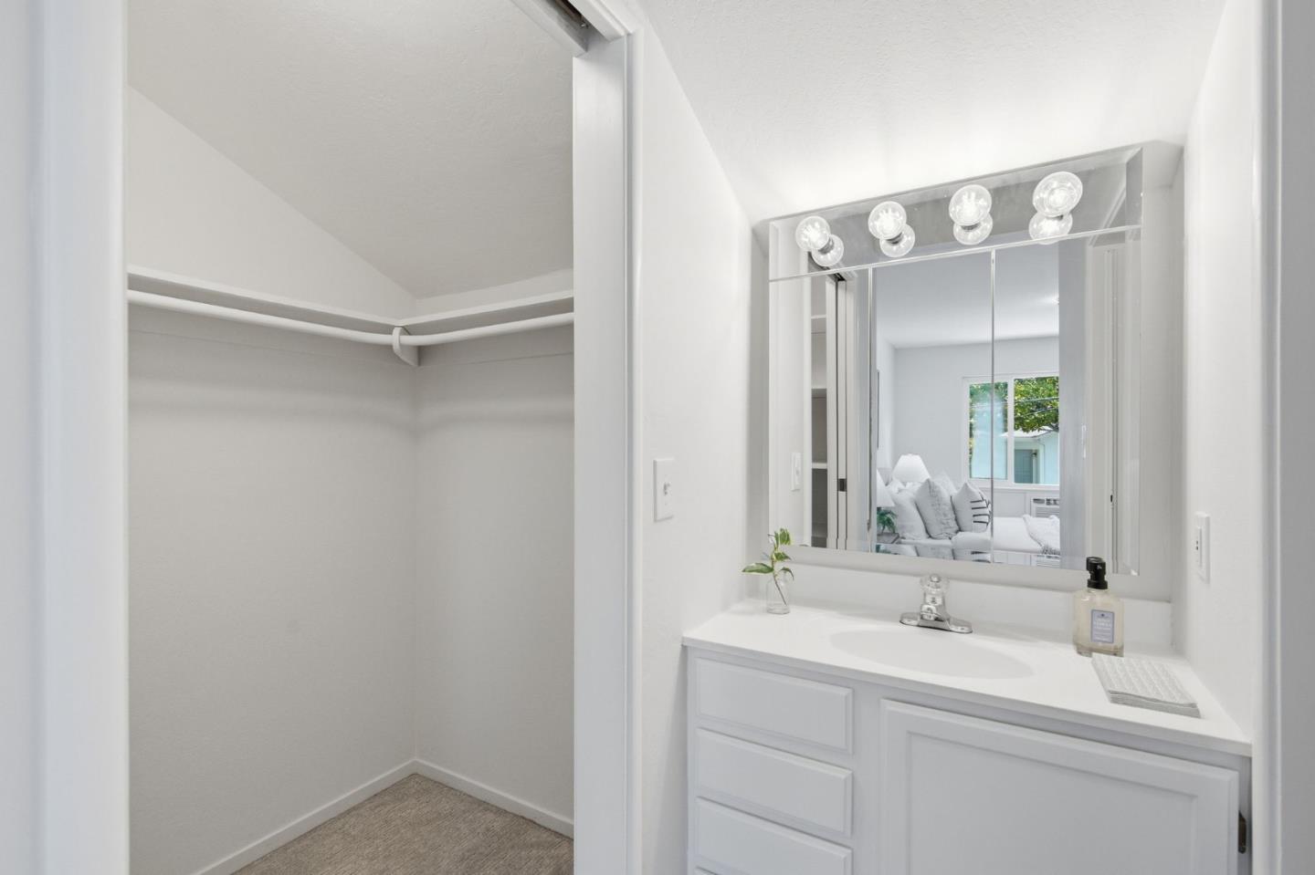 Bright bathroom vanity and mirror beside an open closet with wraparound shelving.