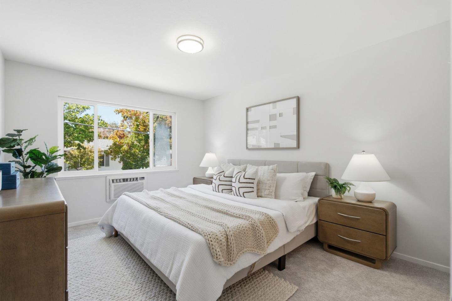 Staged bedroom with a white bed, knit throw, wood nightstands, and a large window.