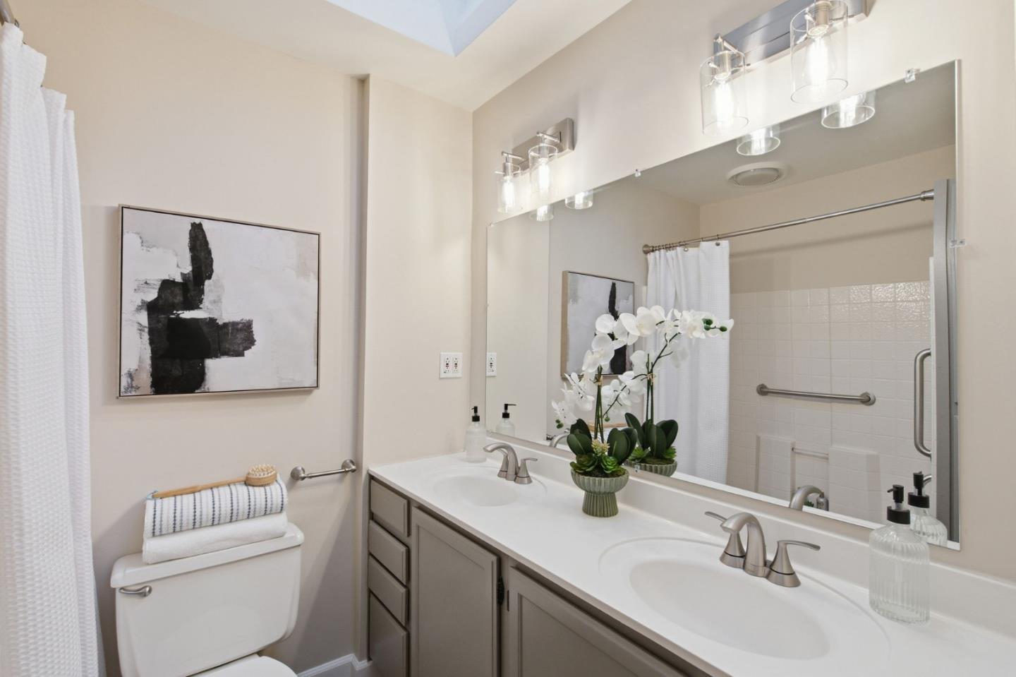 Staged bathroom with a double-sink vanity, large mirror, tiled shower enclosure, and white orchids.